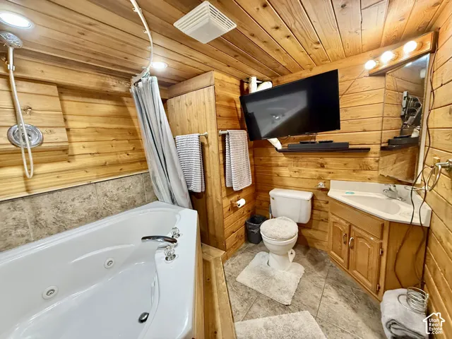 Wood-paneled bathroom featuring a jetted tub, ceramic tile flooring, built-in vanity with single basin sink, and recessed lighting