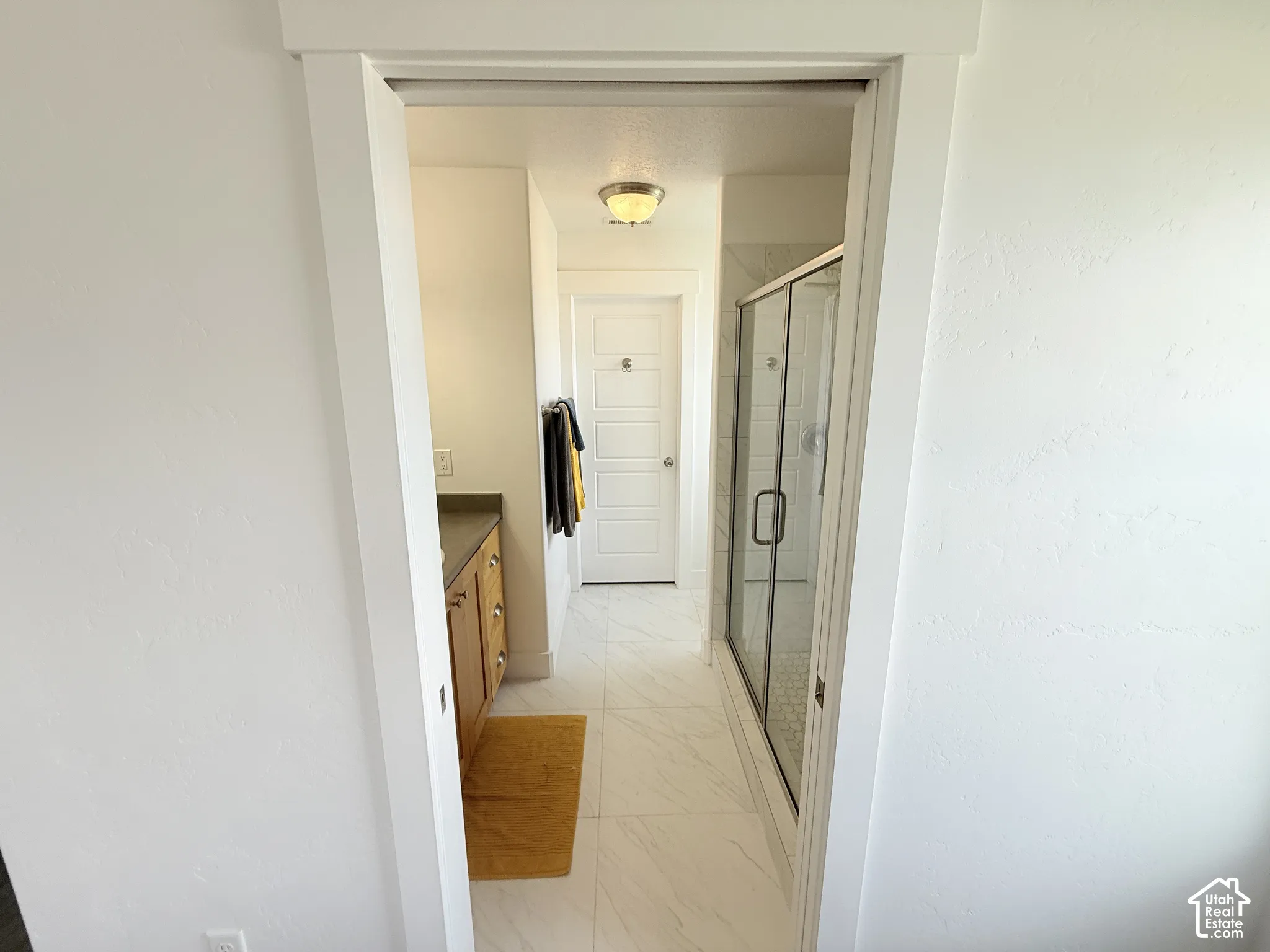 Enclosed glass shower, single vanity with dark countertop, white tile flooring, and white interior doors