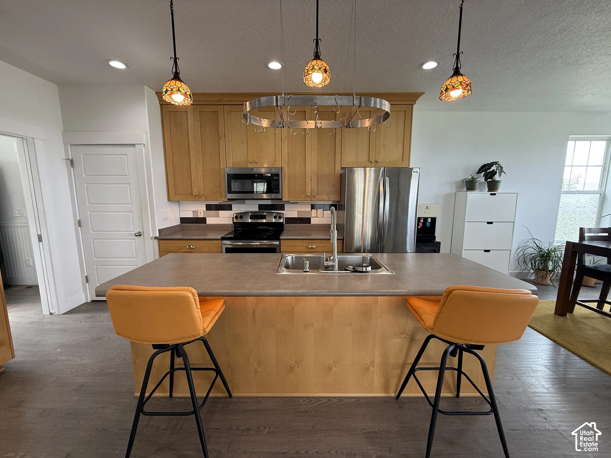 Kitchen featuring wood cabinetry, stainless steel appliances, a multi-tone tile backsplash, and an island with an integrated sink