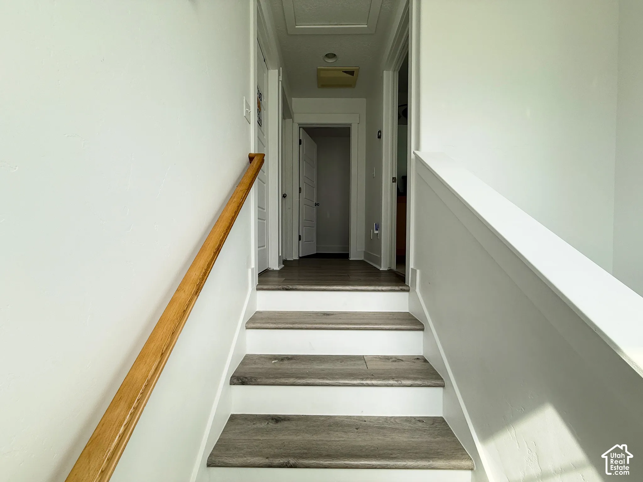 Staircase featuring wood-finish treads, white risers, and a natural wood handrail