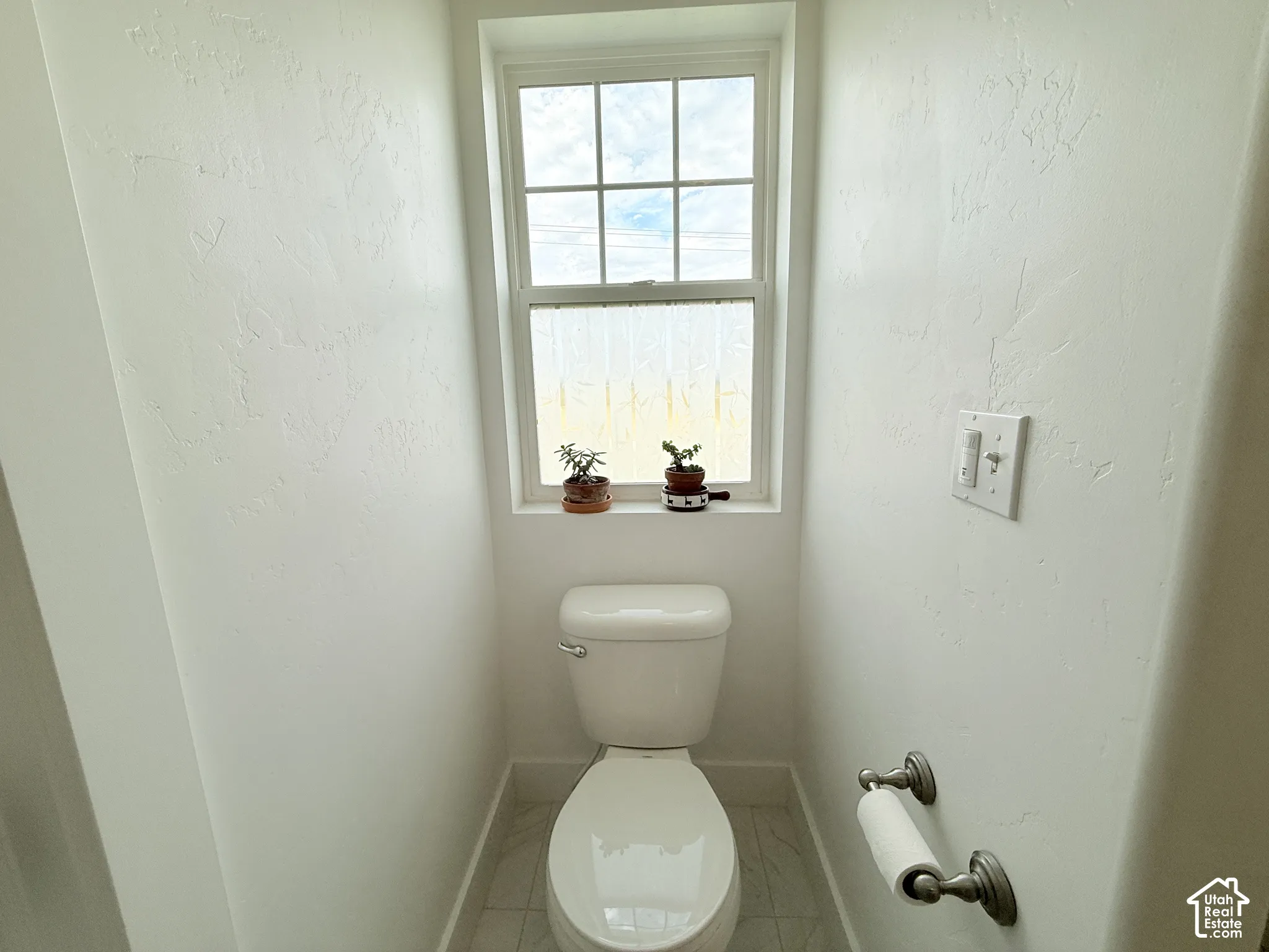 Windowed water closet with textured walls, tile flooring, and brushed nickel hardware
