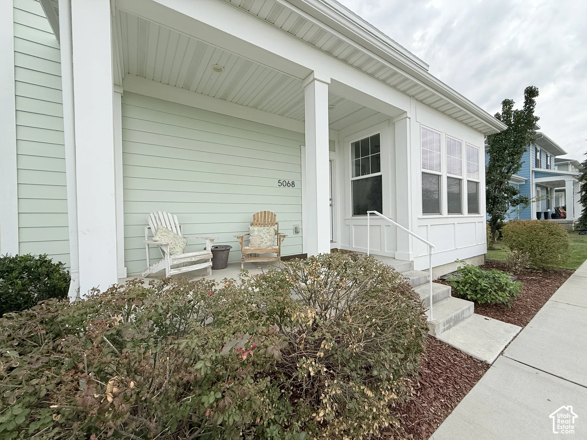 Covered porch with white columns, light green horizontal siding, and a white railing leading to the entry