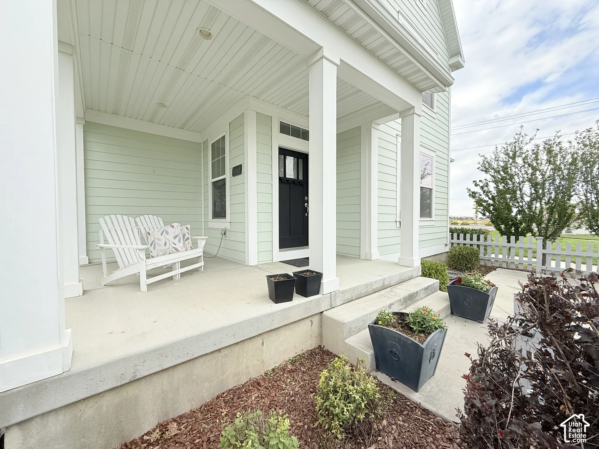 Covered front porch with white columns, light green siding, and a dark entry door