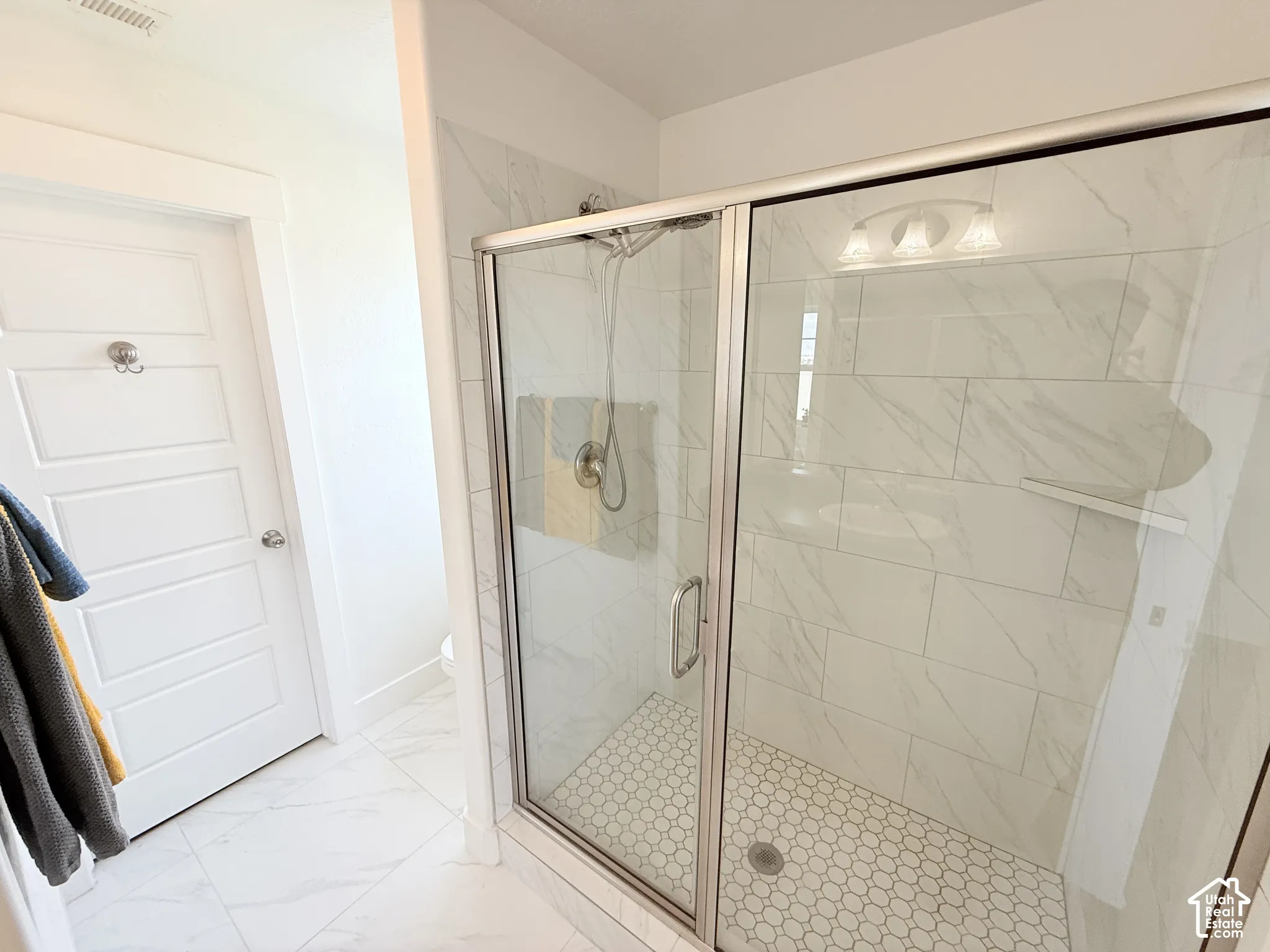 Glass-enclosed shower with a hexagon tile floor, full-height tile surround, and a built-in shelf