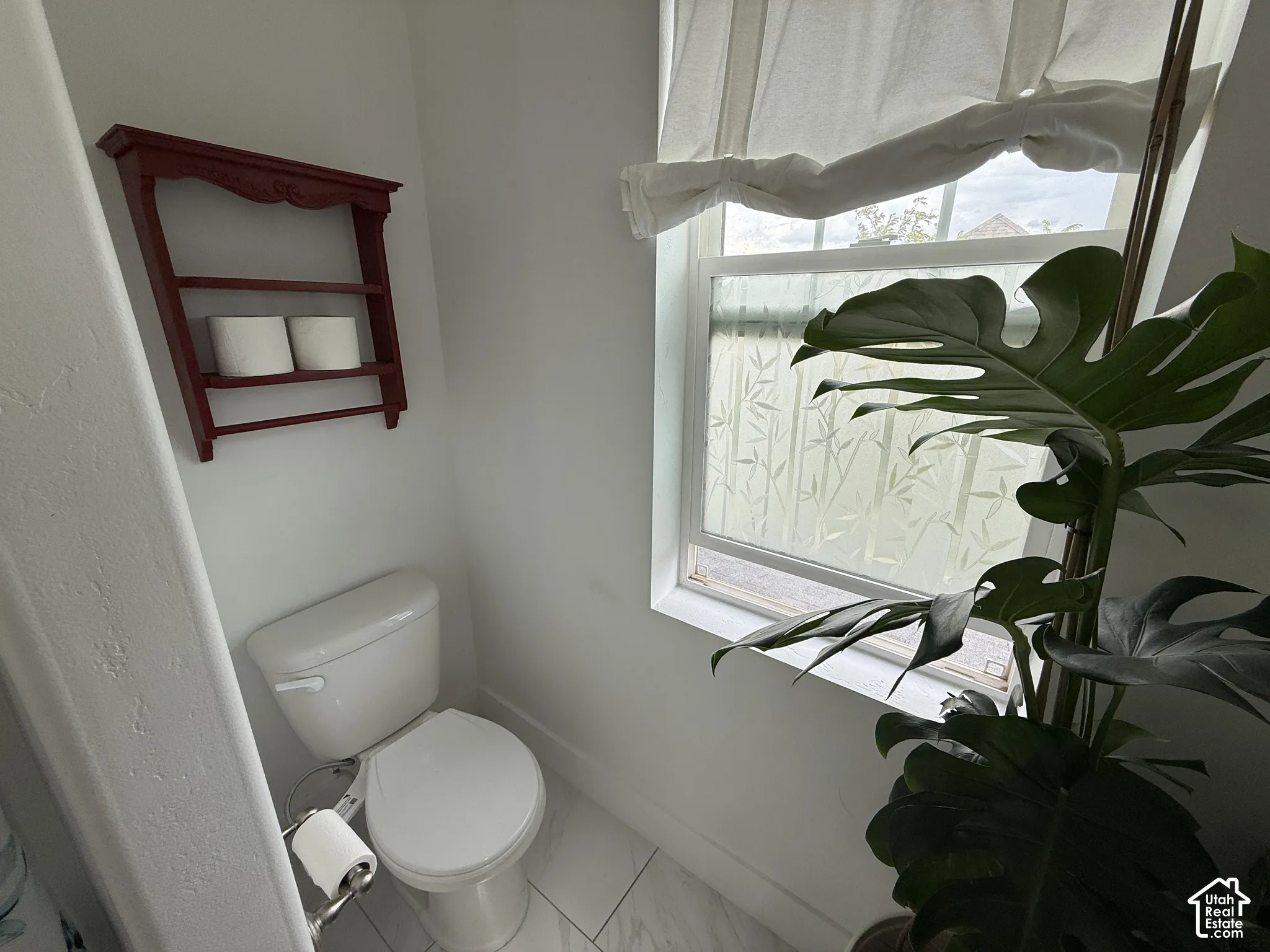 White toilet with a built-in toilet paper holder and a window featuring a decorative privacy film