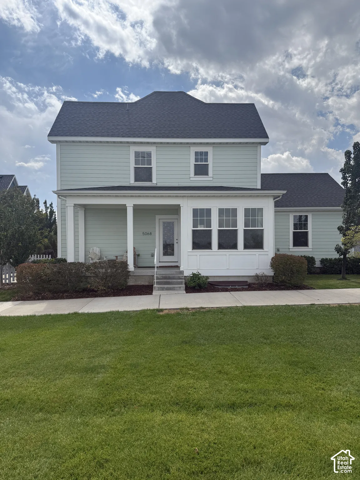 Two-story residence featuring light-colored siding, a dark shingle roof, a covered porch with white columns, and multiple windows