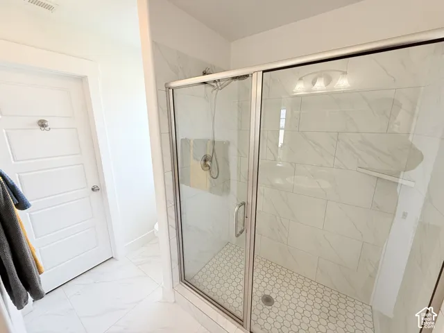 Glass-enclosed shower with a hexagon tile floor, full-height tile surround, and a built-in shelf