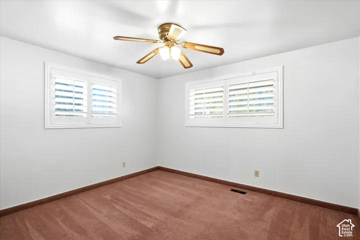 Room featuring two windows with white plantation shutters, a ceiling fan with integrated lighting, and carpeted flooring