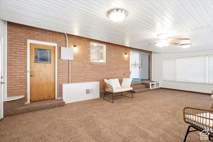 Brick accent wall, sliding glass door, multiple ceiling light fixtures, large windows with blinds, and built-in shelving
