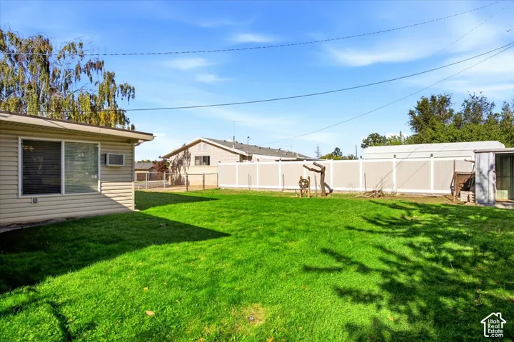 Expansive green lawn, durable vinyl siding, sliding glass door, white privacy fencing, and an outbuilding
