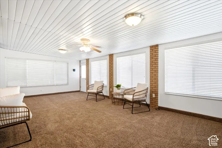 Carpeted floor with exposed brick accents and white paneled ceiling