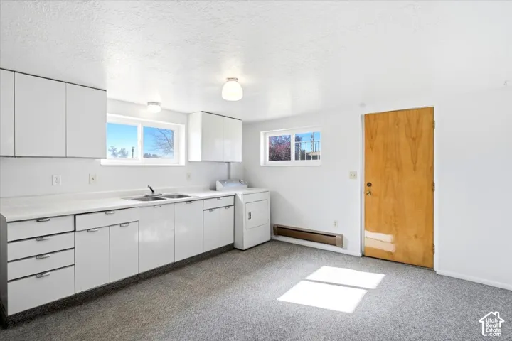 White cabinetry with chrome hardware, dual-basin sink, white countertops, two windows, and textured white ceiling