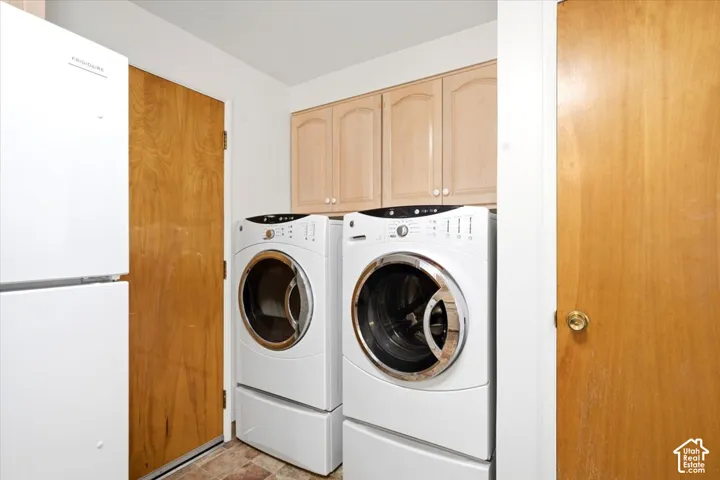 Laundry area with two front-load appliances and upper cabinetry