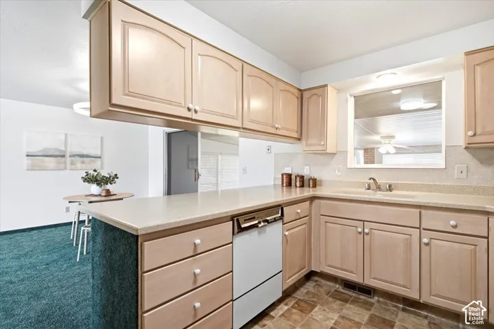 Kitchen featuring light wood-finish cabinetry, light-toned countertops, and a white dishwasher