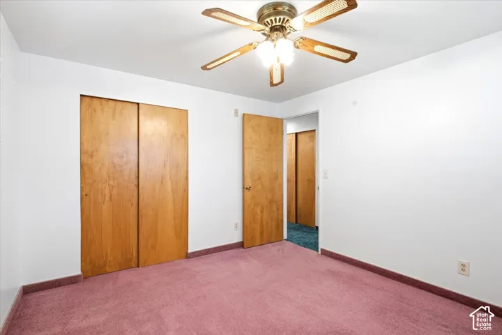 Ceiling fan light fixture with wood-finish blades, white walls, wood-finish bi-fold closet doors, and pink carpet flooring