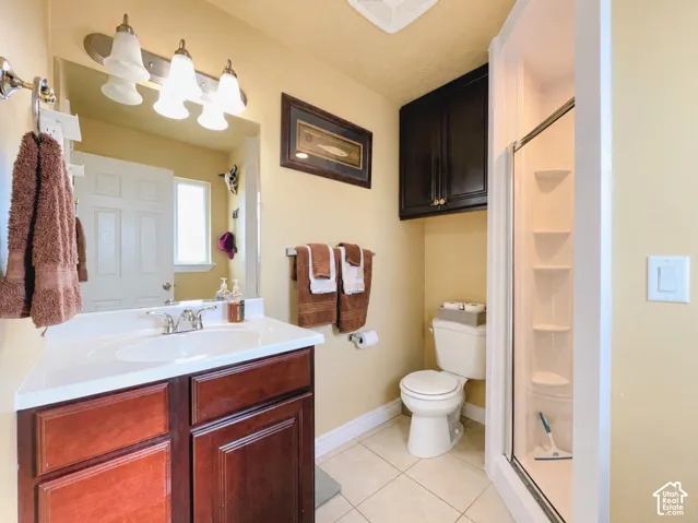 Vanity with integrated sink, wood-finish cabinetry, chrome faucet, tiled flooring, and a shower with a clear enclosure