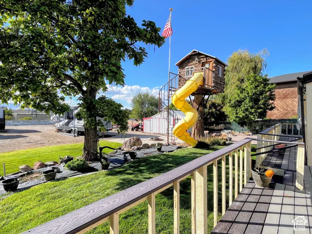 Expansive lawn area with a mature tree, a built-in treehouse featuring a spiral slide, and a durable composite deck with railings