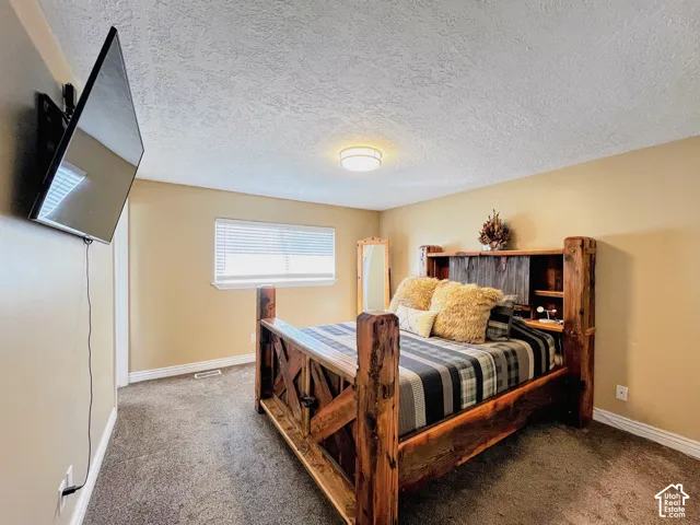 Wall-mounted television, neutral wall color, window with blinds, overhead flush-mount lighting, and textured ceiling