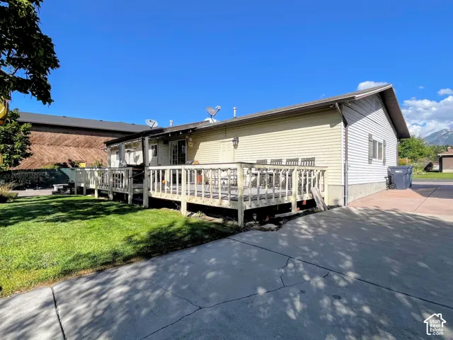 Expansive wooden deck, green lawn, white vinyl siding, mountain backdrop, and concrete driveway