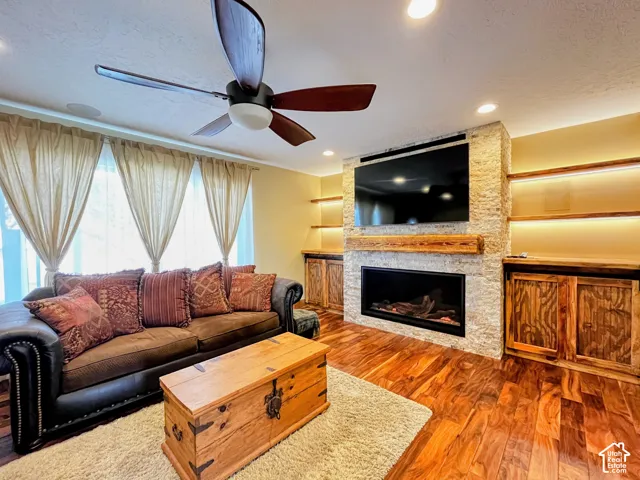 Built-in fireplace with stone surround, wood-finish flooring, built-in shelving with accent lighting, recessed ceiling lighting, and a ceiling fan