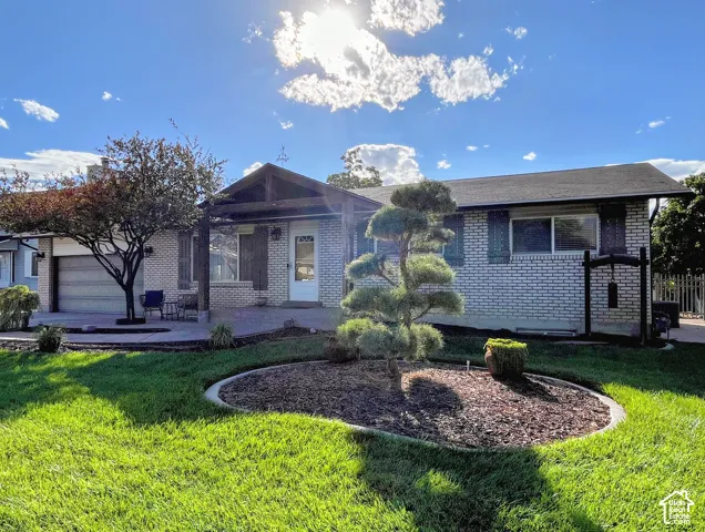 White brick exterior with dark shutters, front patio, attached garage, and landscaped front yard