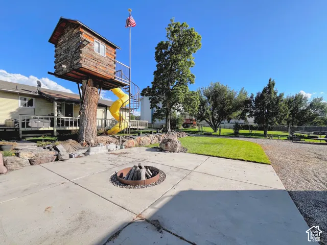 Exterior concrete patio with a built-in fire pit, manicured lawn, and a treehouse featuring a spiral staircase and slide