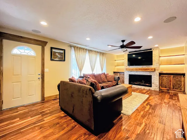 Living area with wood-finish flooring, a stone-clad fireplace, and built-in shelving with integrated lighting