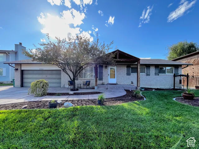 Brick exterior with a covered entry, attached garage, concrete driveway, and landscaped front yard with a mature tree