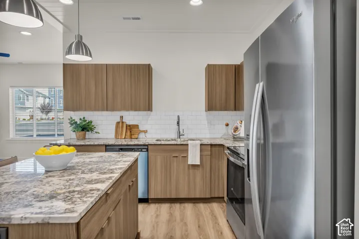 Kitchen featuring wood-finish cabinetry, stainless steel appliances, speckled stone countertops, and white subway tile backsplash