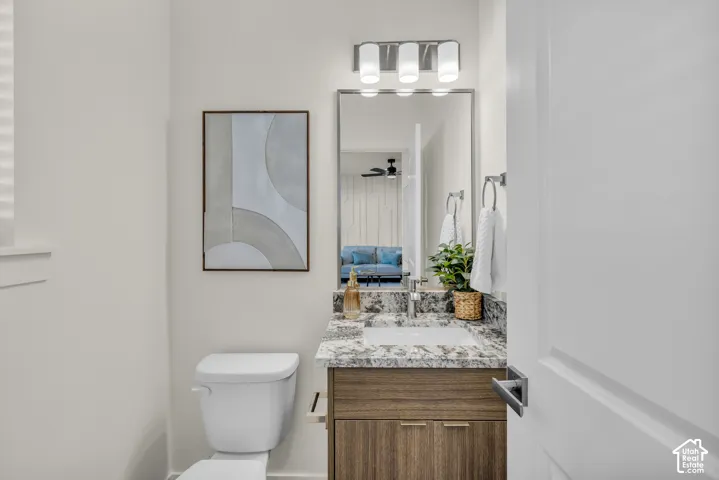 White toilet with a wood-finish vanity, stone countertop, and an undermount sink