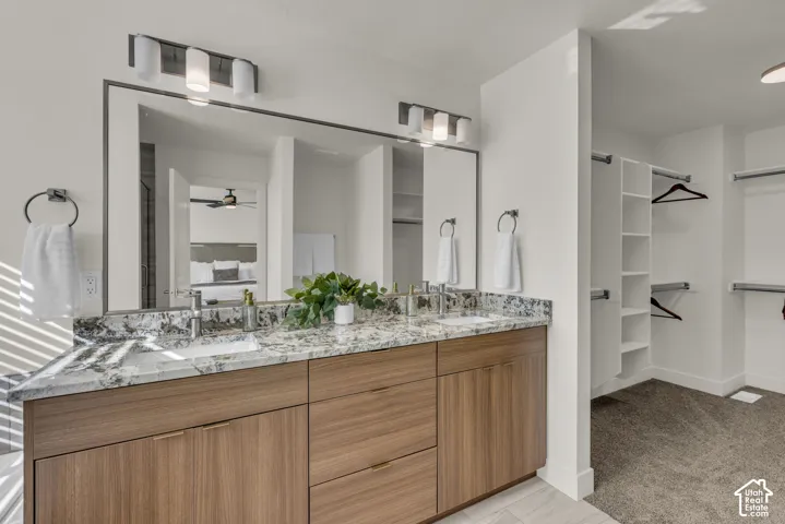 Double vanity with stone countertop, wood-finish cabinetry, dual undermount sinks, and built-in closet shelving