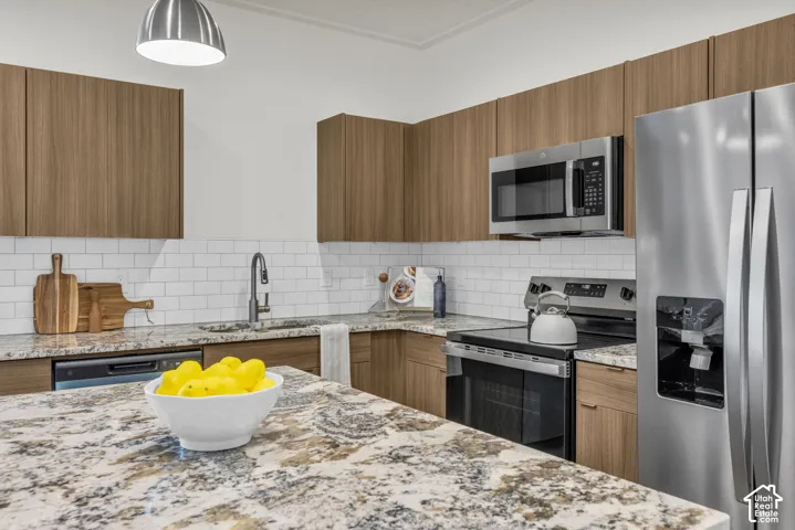 Kitchen featuring wood-finish cabinetry, stone countertops, subway tile backsplash, stainless steel appliances, and a stainless steel sink with a gooseneck faucet