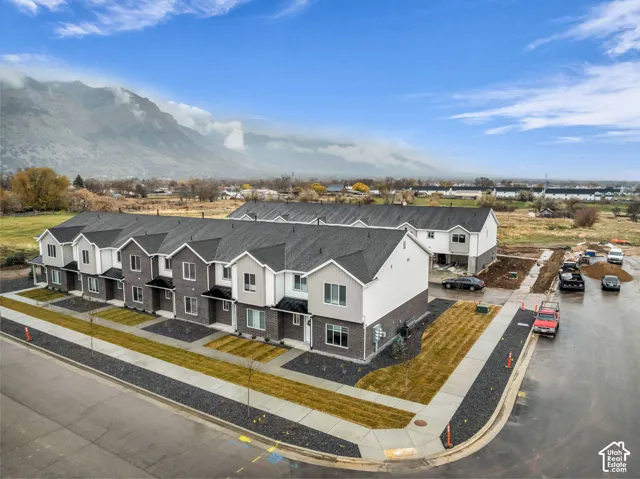 Newly constructed townhomes with mixed material exteriors, dark shingle roofing, paved street frontage, and manicured landscaping