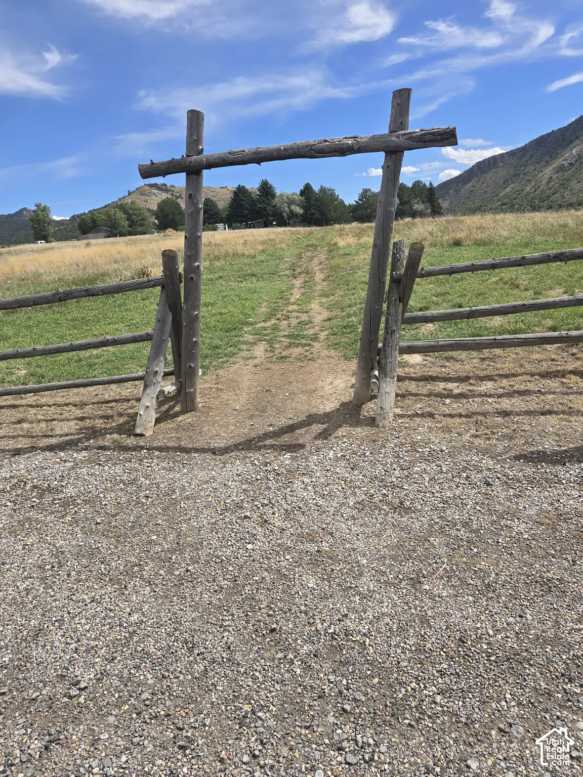 Gravel foreground with a rustic wooden gate and fence opening to a grass and dirt path