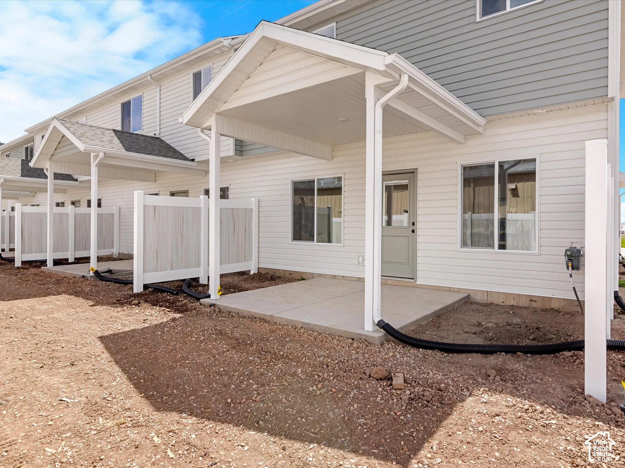 Rear exterior featuring white horizontal siding, covered concrete patio, light gray door, multiple windows, and partial privacy fencing