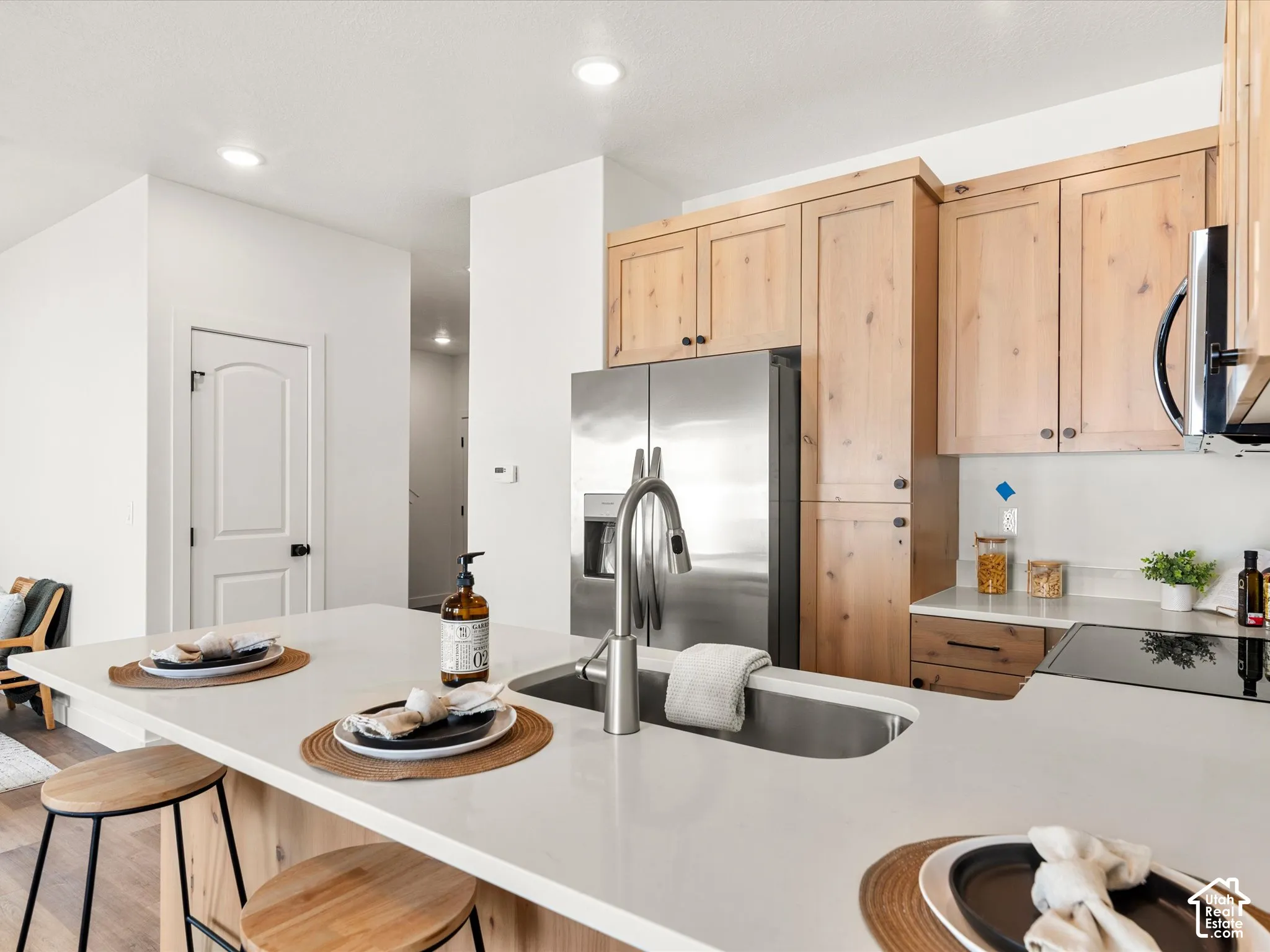 Kitchen featuring a stainless steel refrigerator, neutral countertops, wood-finish cabinetry, built-in cooktop, and an undermount sink with a gooseneck faucet
