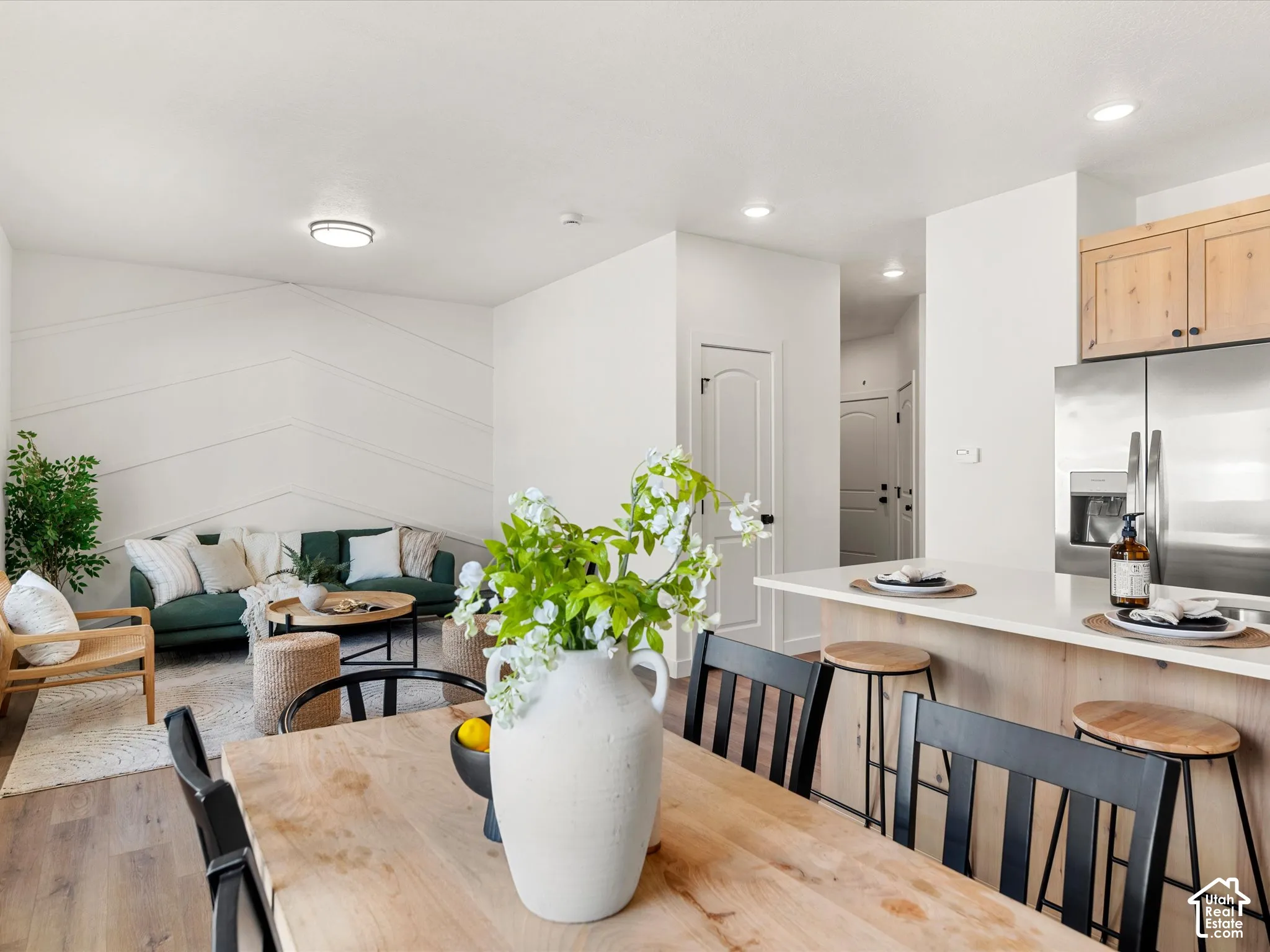 Open-concept living space featuring wood-finish flooring, a kitchen island with seating, stainless steel appliances, and a decorative accent wall