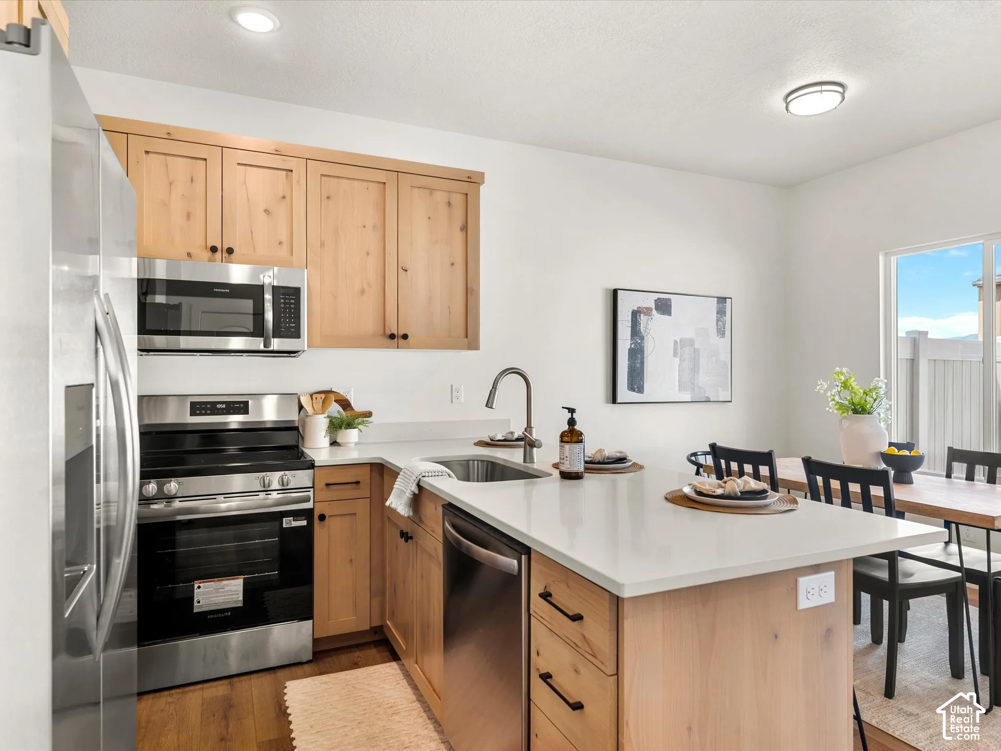 Stainless steel appliance suite, light wood-finish cabinetry, white countertop surfaces, and a built-in kitchen island
