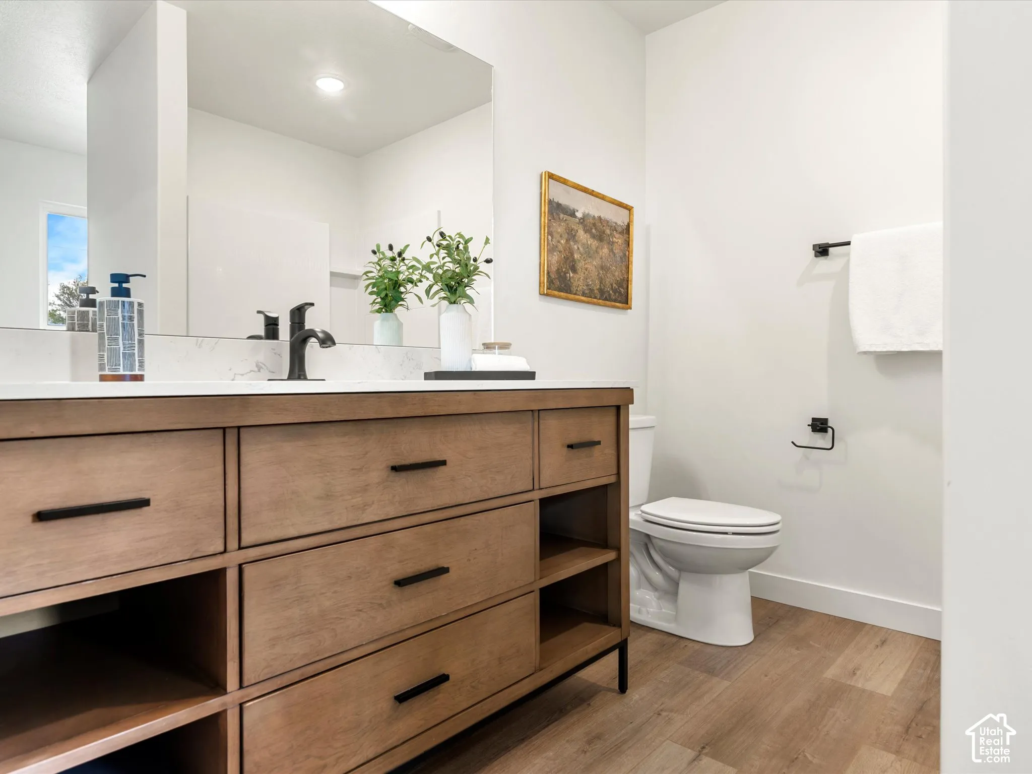 Wood-finish flooring, white walls, and a wood-tone vanity with black hardware