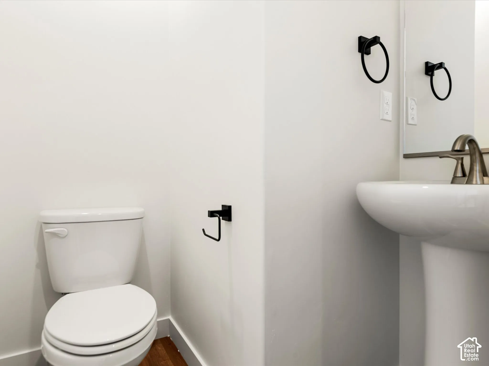 White pedestal sink with brushed nickel faucet, wall-mounted mirror, and black towel ring