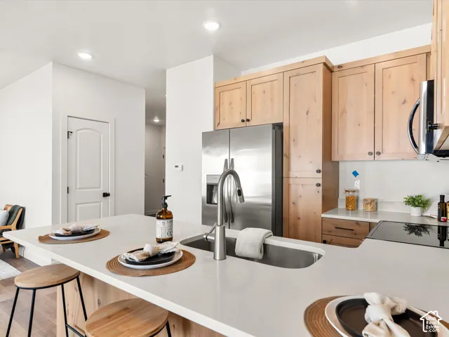 Kitchen featuring a stainless steel refrigerator, neutral countertops, wood-finish cabinetry, built-in cooktop, and an undermount sink with a gooseneck faucet
