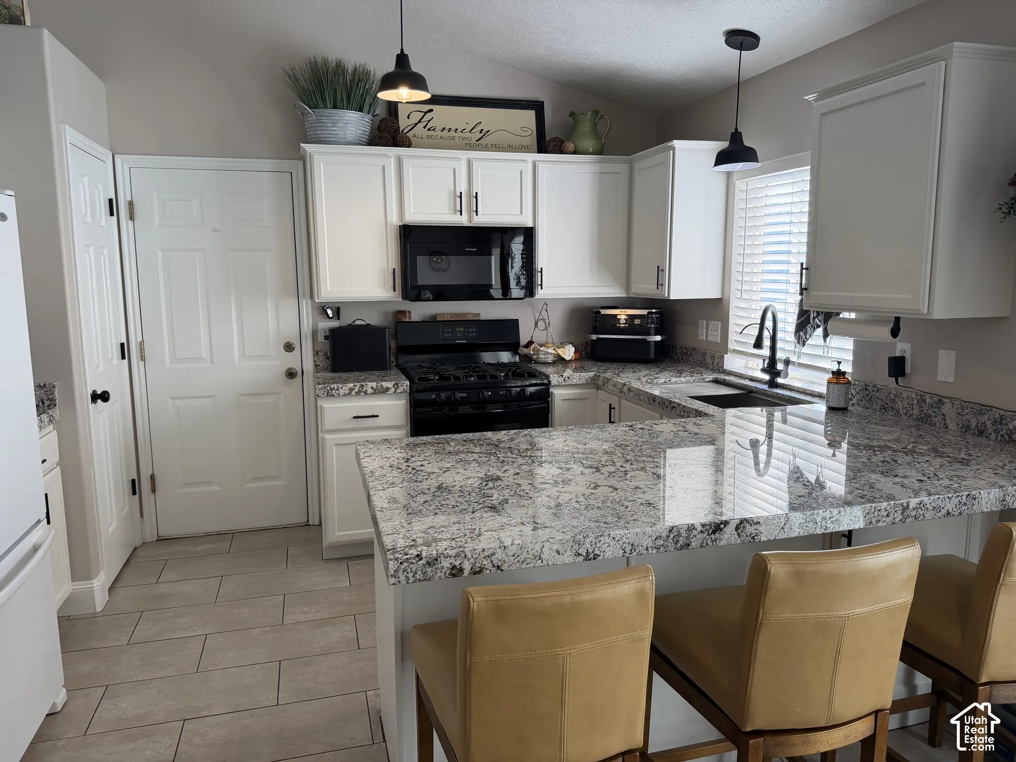 White cabinetry with black hardware, black appliances, light-colored countertops, dark pendant lighting, and light-toned tile flooring