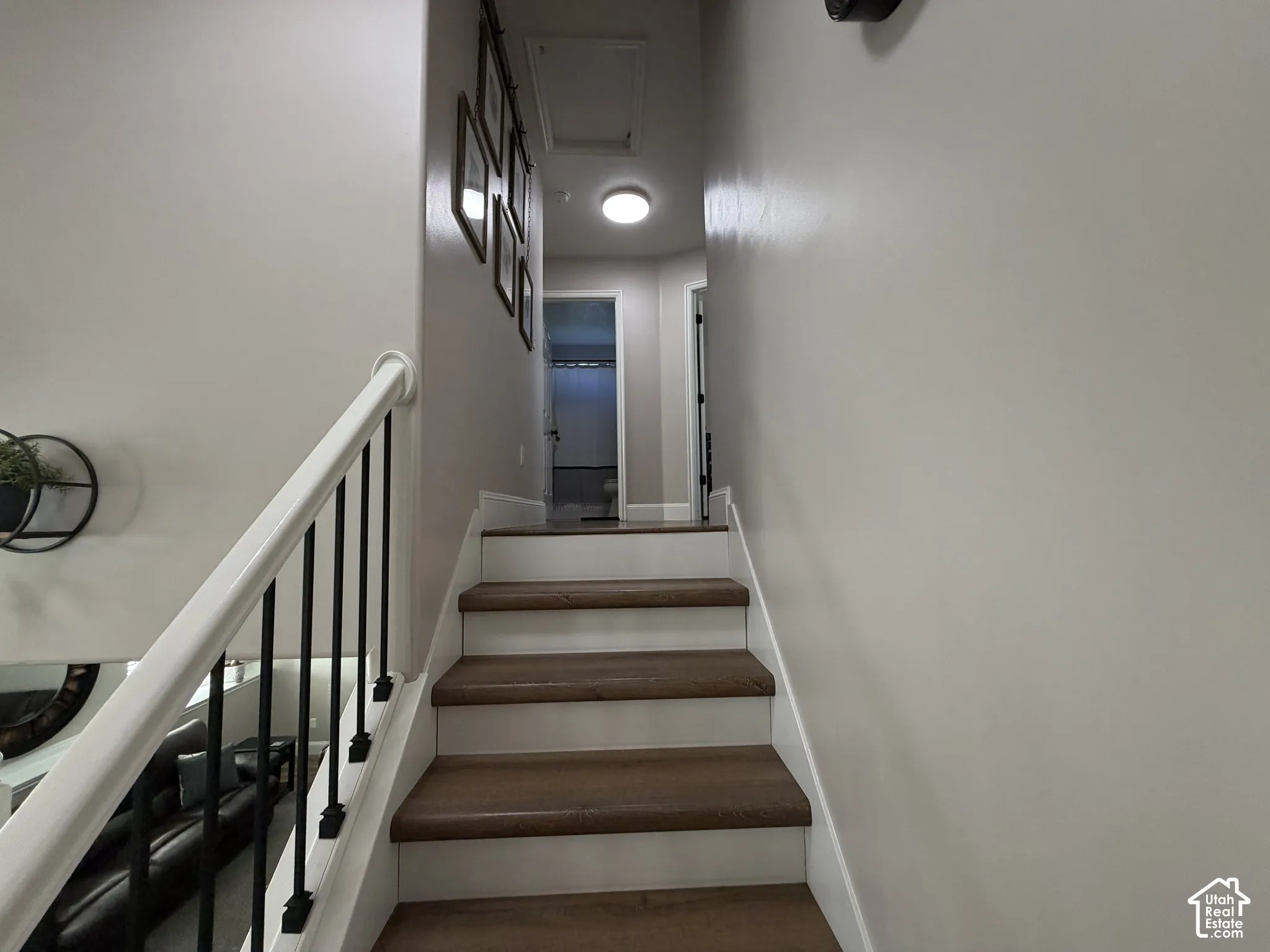 Staircase featuring wood-finish treads, white risers, and a white handrail with black balusters