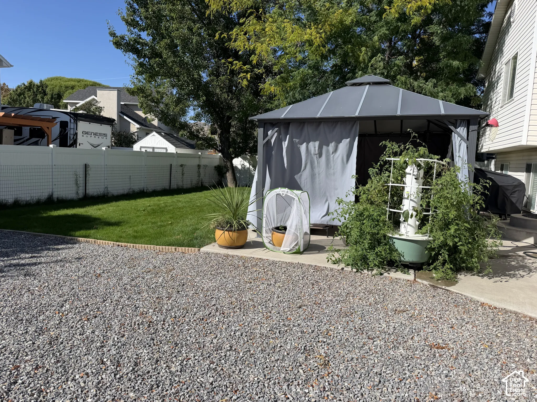 Gravel ground cover, concrete patio, privacy fence, manicured lawn, and mature trees