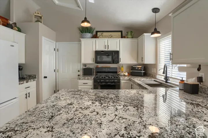 Kitchen featuring a large island with stone countertops, white cabinetry, and black pendant lighting