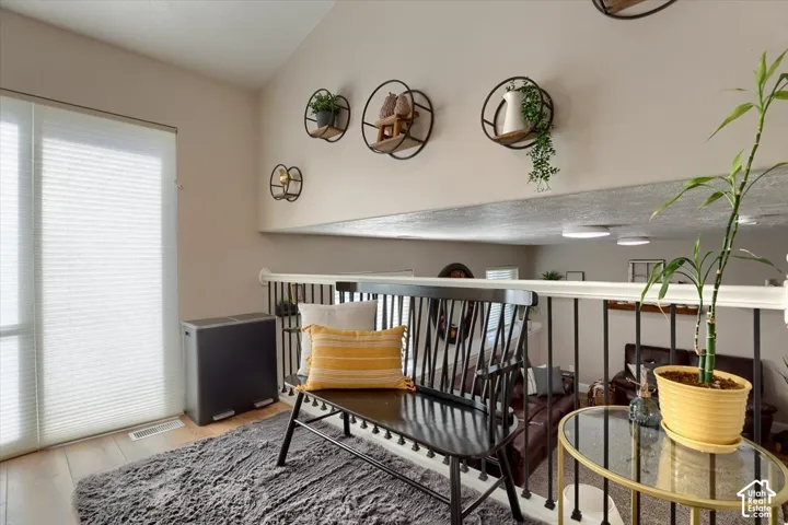 Vaulted ceiling with decorative wall shelving, hardwood-finish flooring, and white window blinds