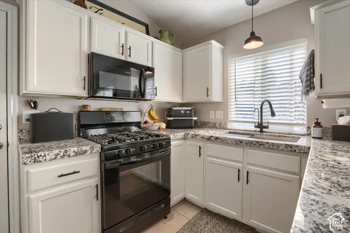 White cabinetry with black hardware, black gas range, built-in black microwave, and speckled countertops