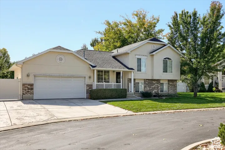 Stucco exterior with brick accents, two-car garage, established landscaping, and a covered porch