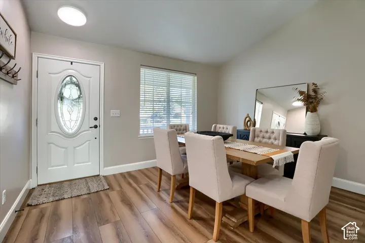 Wood-finish flooring, white entry door with decorative glass insert, window with blinds, vaulted ceiling, and recessed lighting