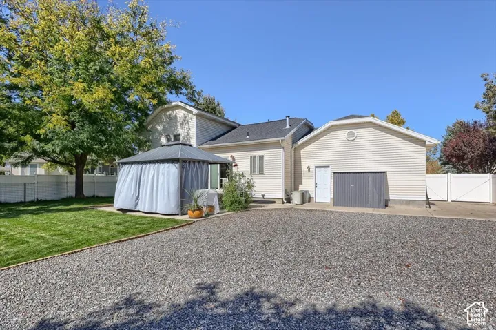 Gravel driveway leading to a two-story residence with a side-entry garage, featuring a white vinyl fence and a lawn area